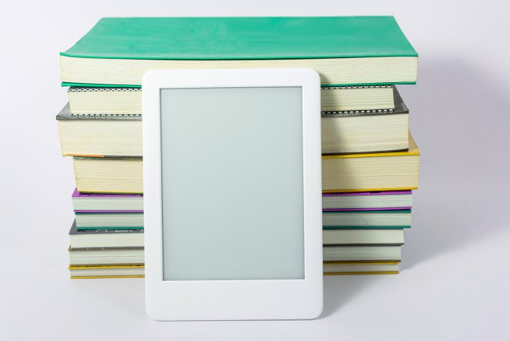 An e-reader sitting next to a stack of books