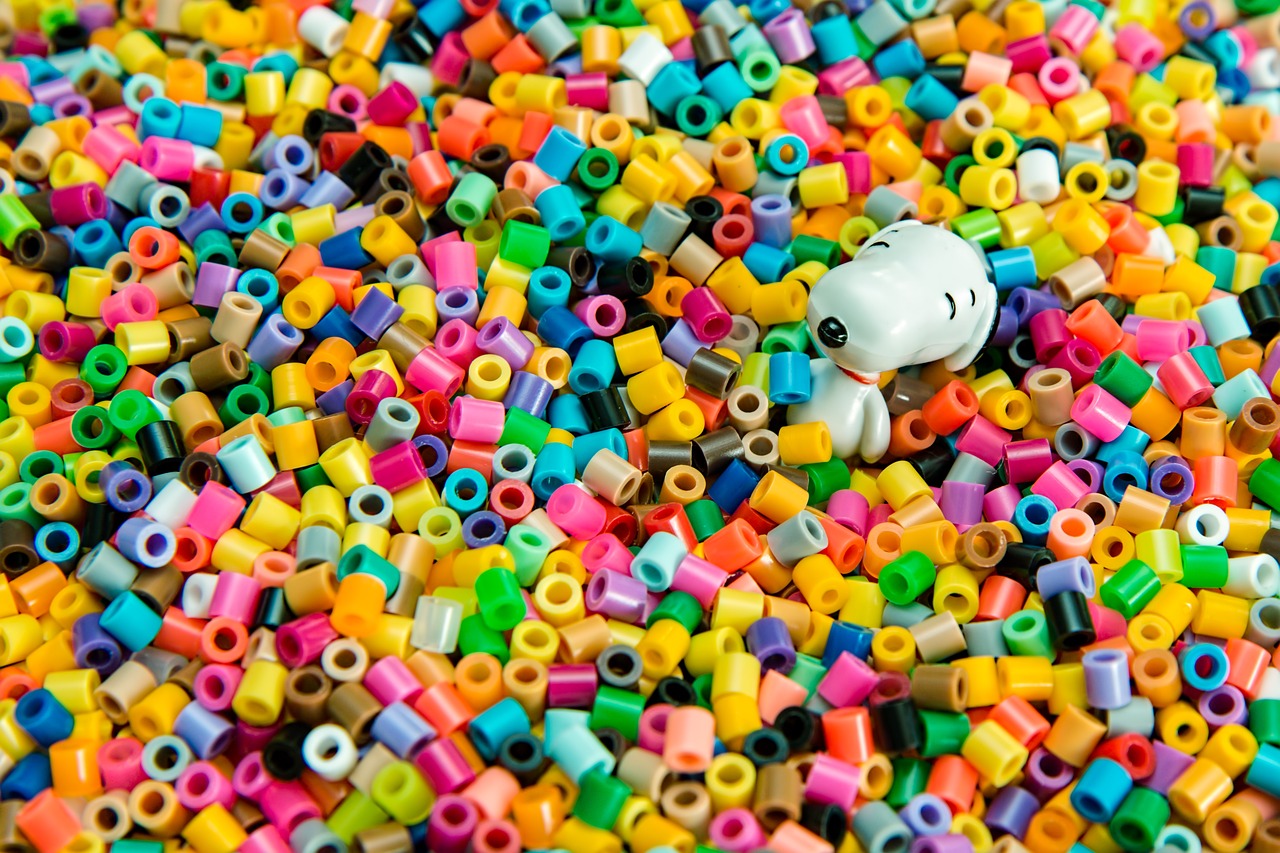 A snoopy toy sitting half submerged in a pool of colorful plastic beads. Snoopy is a white dog with a red collar and black ears and a black nose.