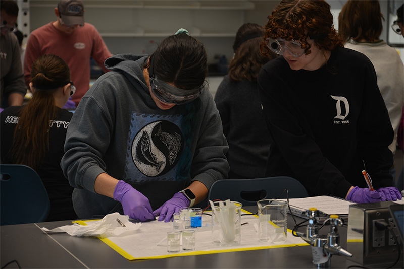 Two students working with beakers wearing surgical gloves.