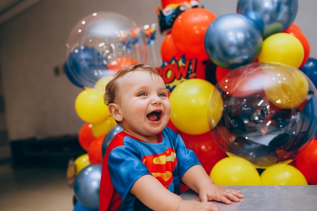 boy wearing superhero outfit smiling with balloon arrangement in background