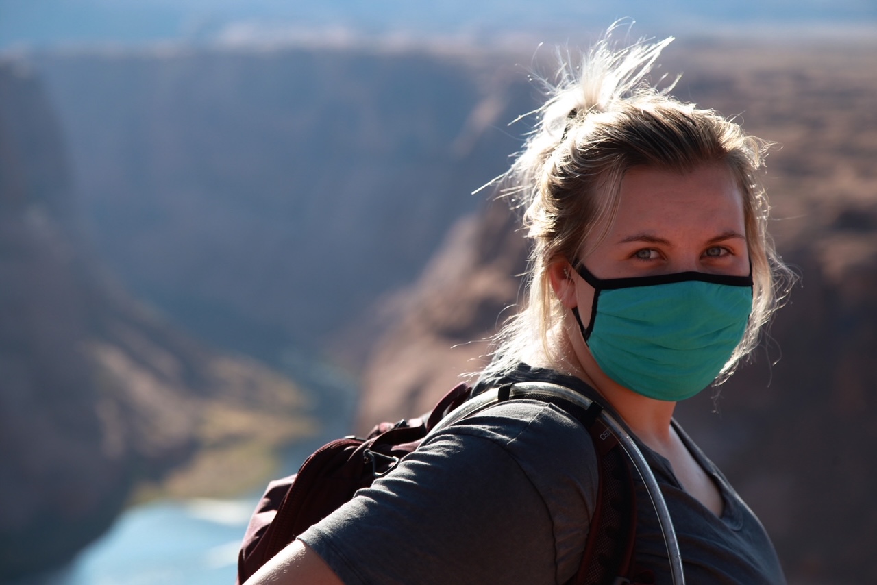 A girl with a mask looking at the camera whith a canyon blurred out behind her.