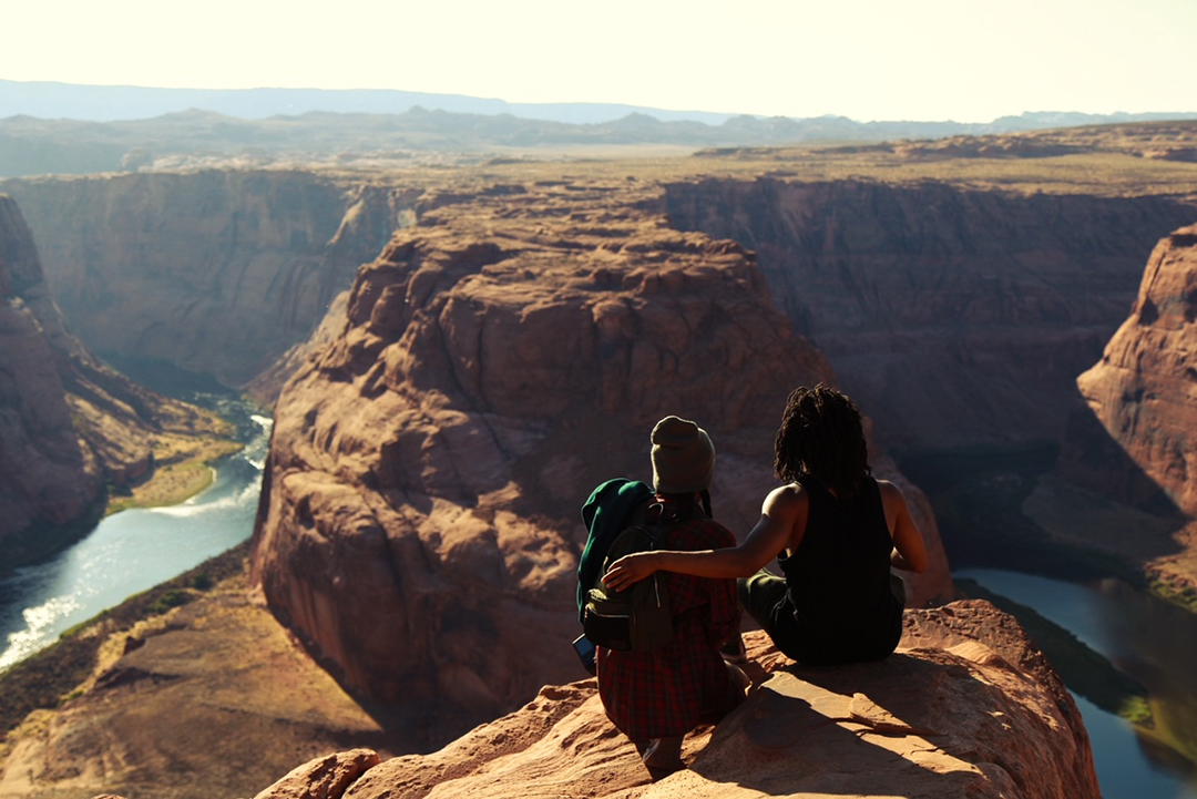 A brother and sister sit on the edge of a cliff at Horseshoe Bend.