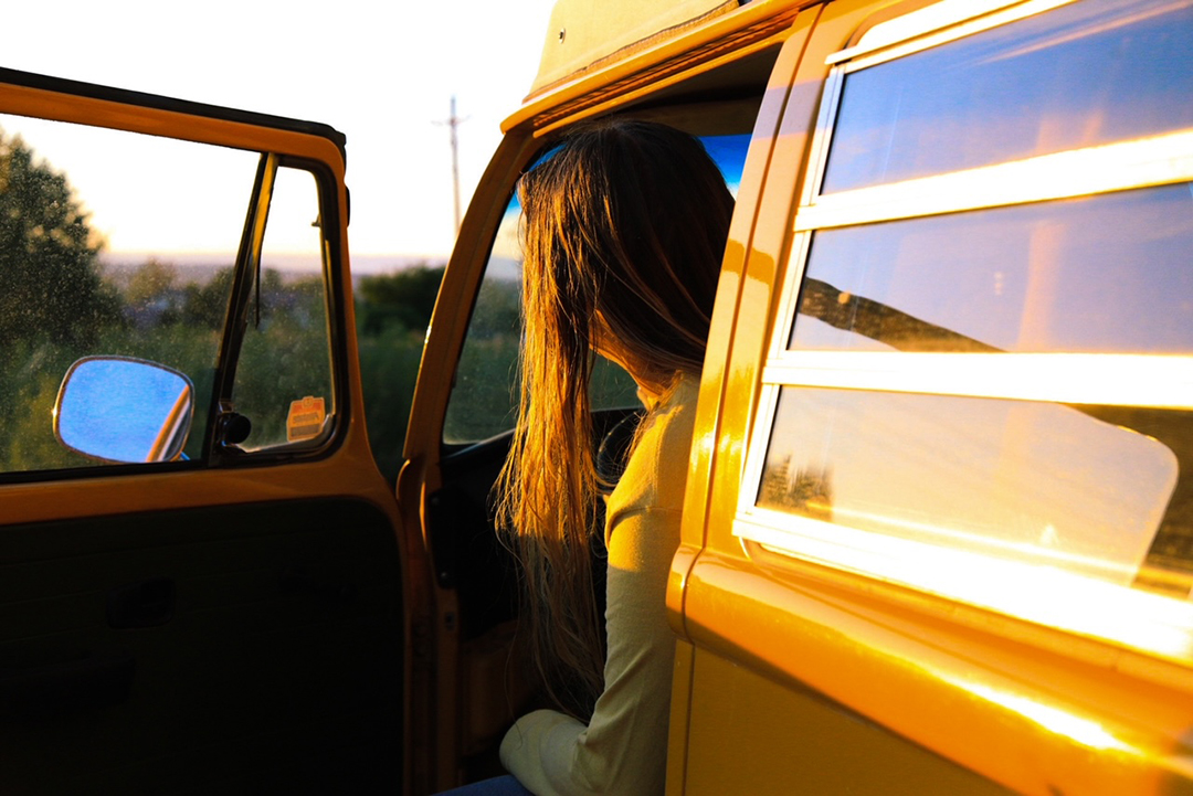 Looking over the shoulder of a girl looking ahead as she opens a yellow van door.