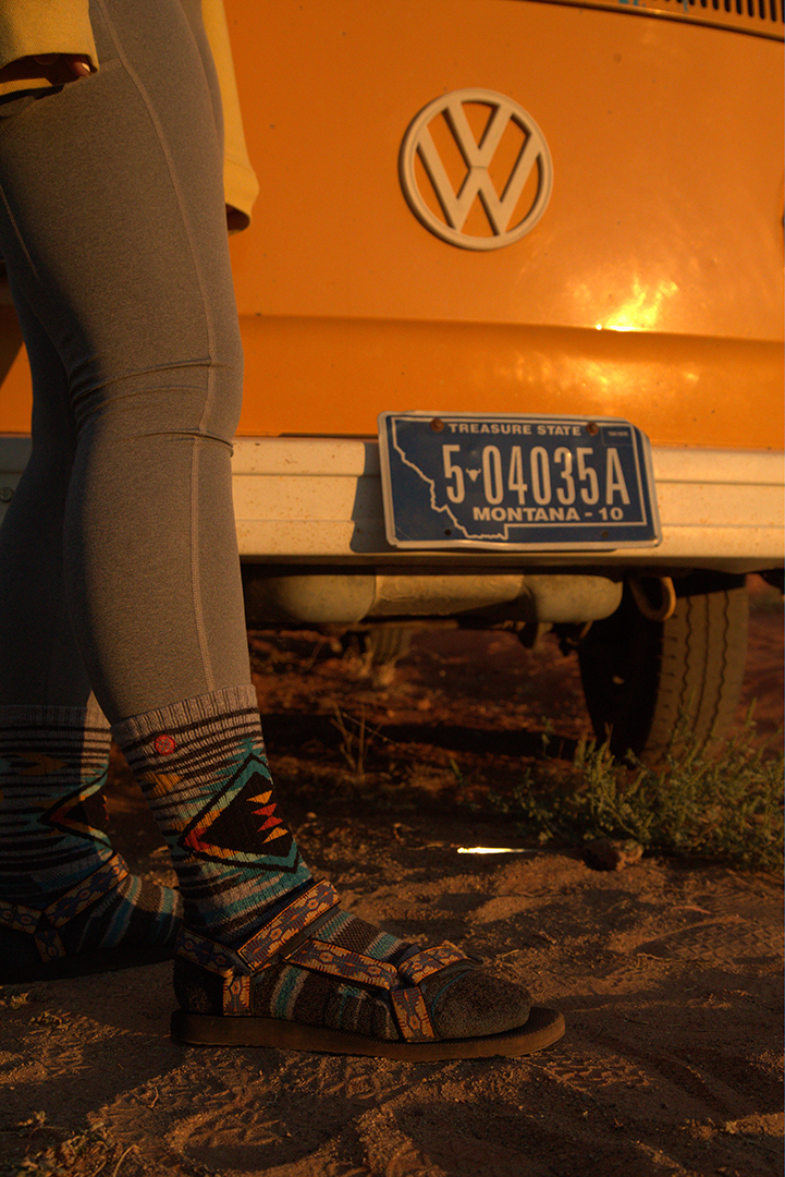 A close up on a person's legs and feet while standing infront of a yellow van.