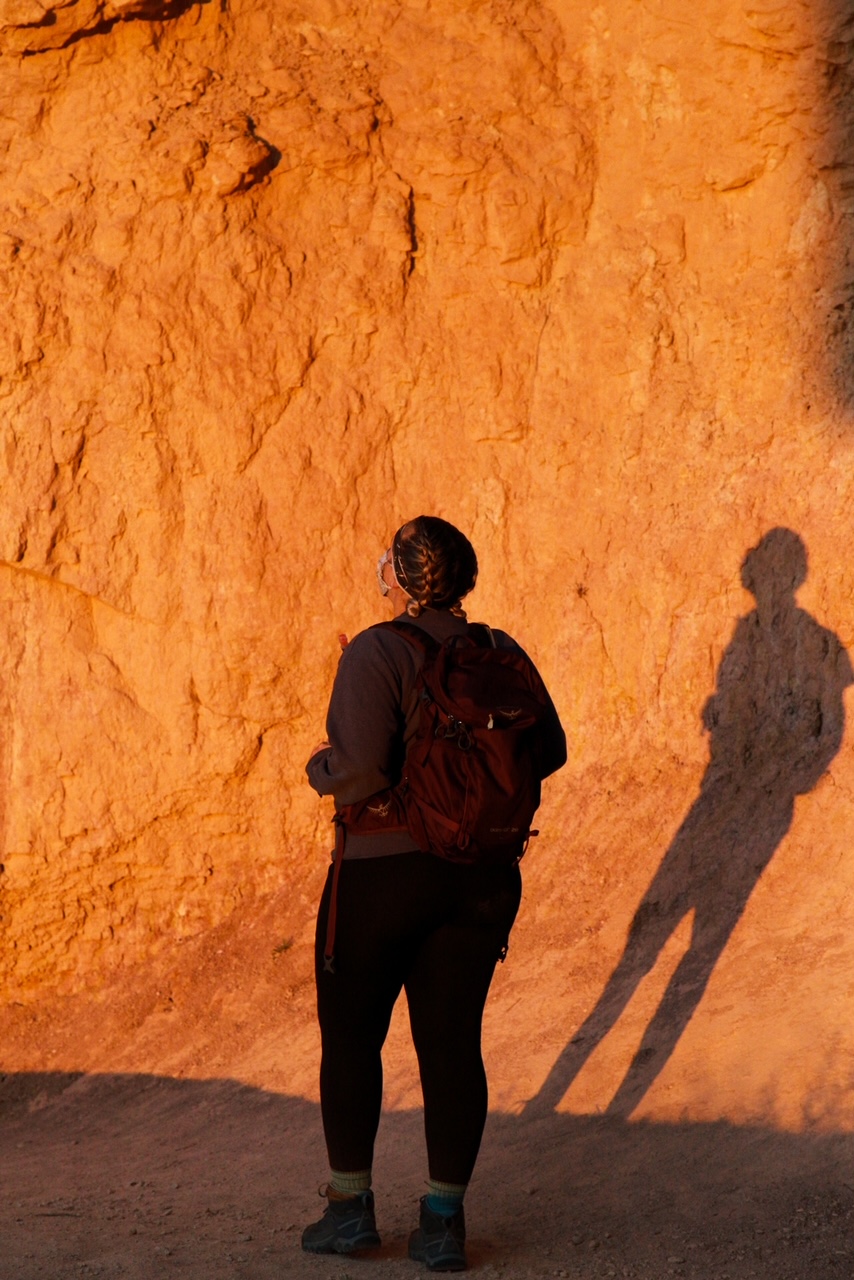 A hiker stands, looking up at the canyong that they are in during the peak of sunrise.