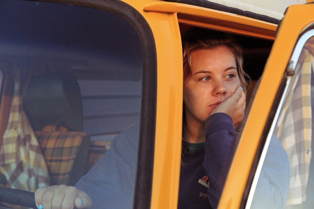 A girl looking off in the distance while sitting in a yellow van.