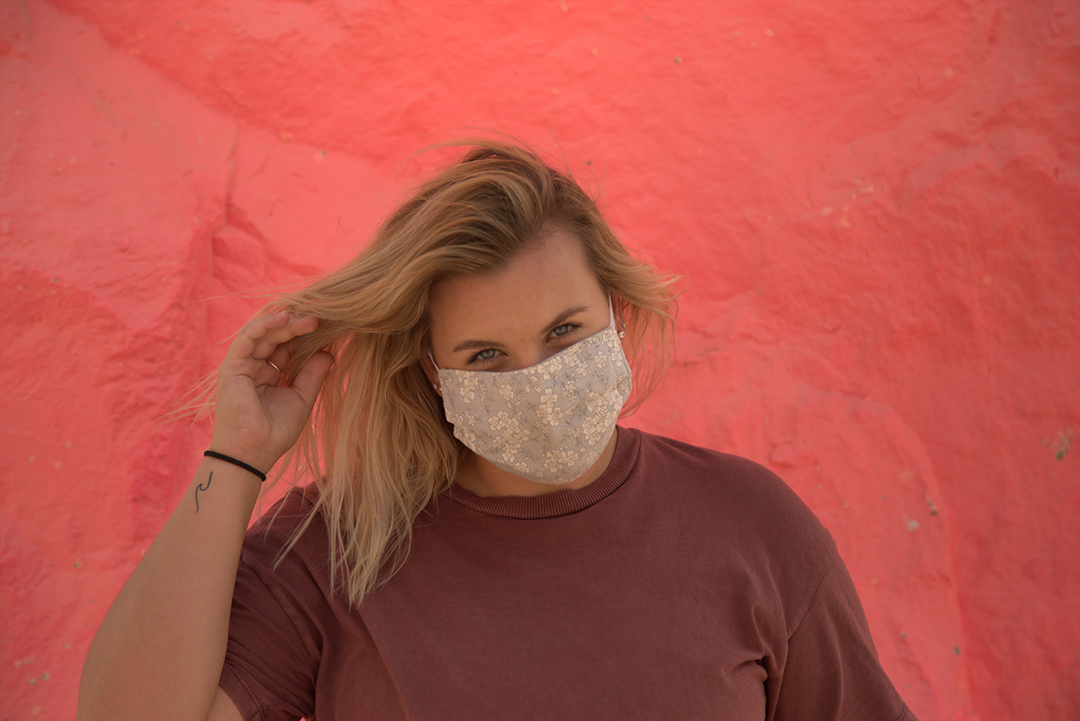 A girl stands in front of a pink rock looking at the camera.