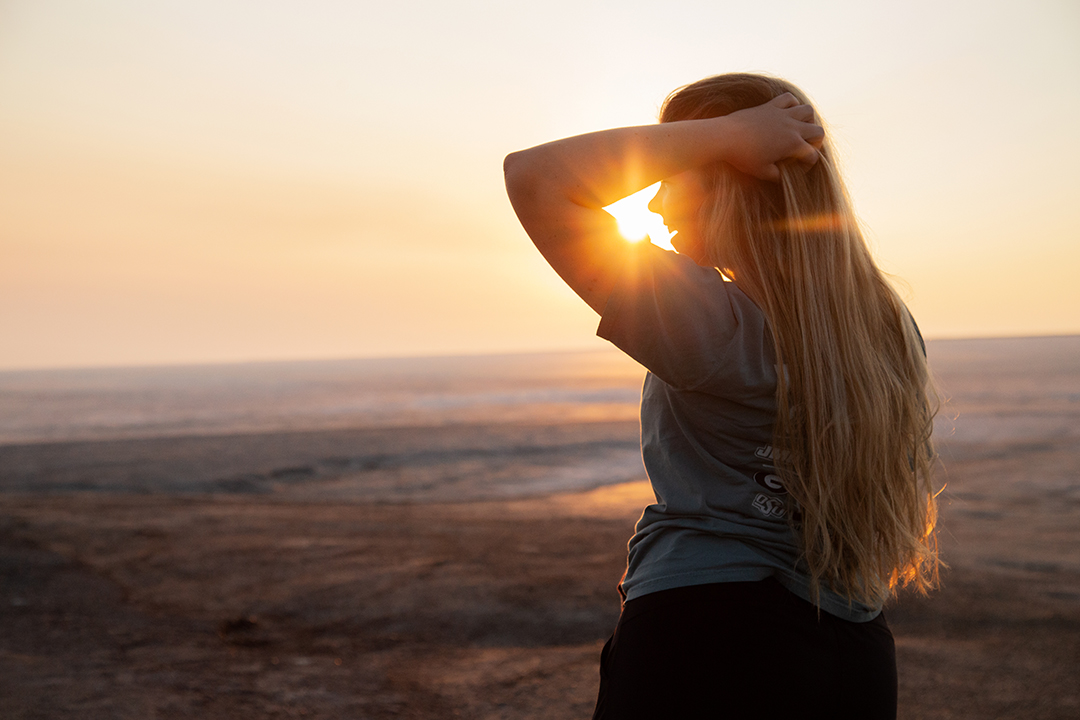 A girl looking off to the left with the sunrising in the background.