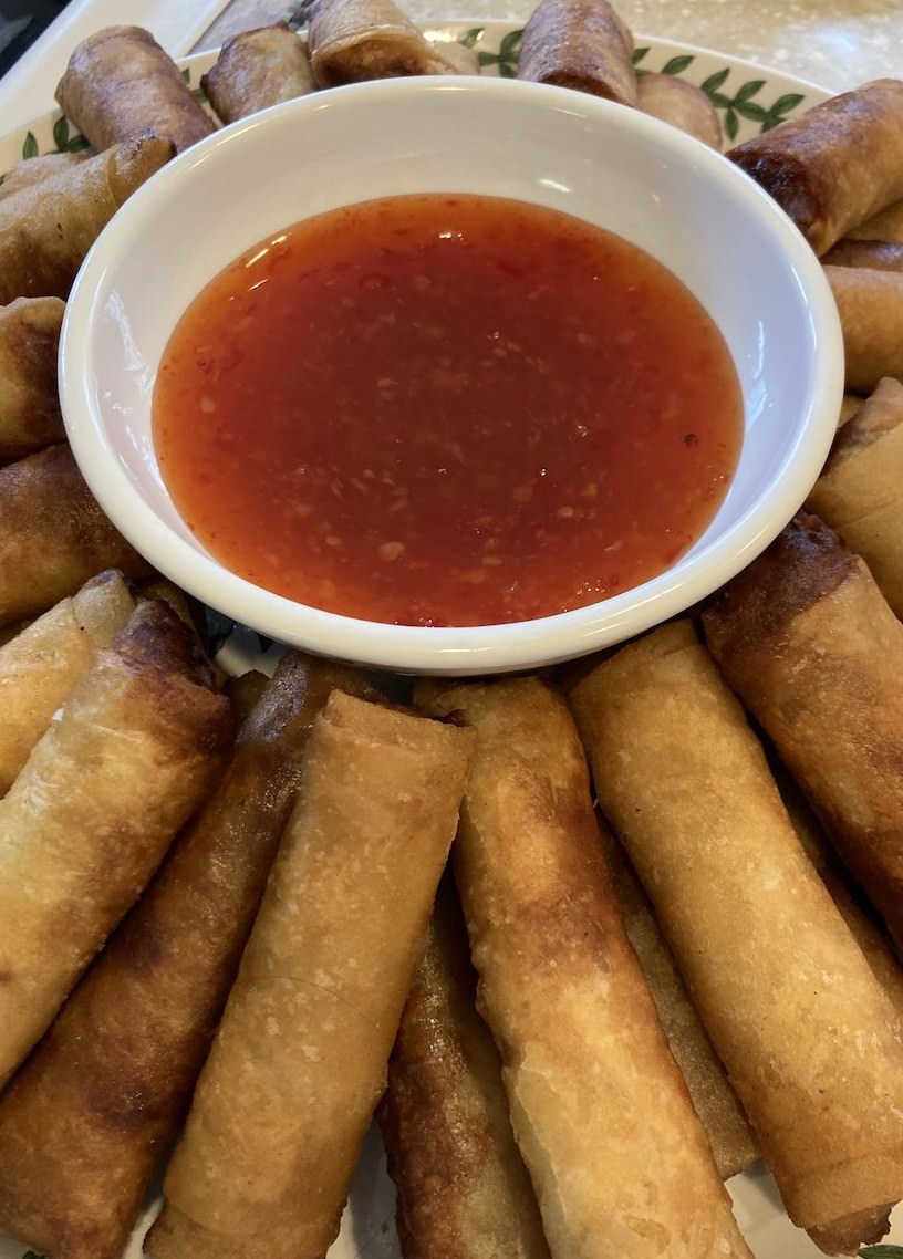 A picture of lumpia on a plate with a bowl of sweet chili sauce in the middle