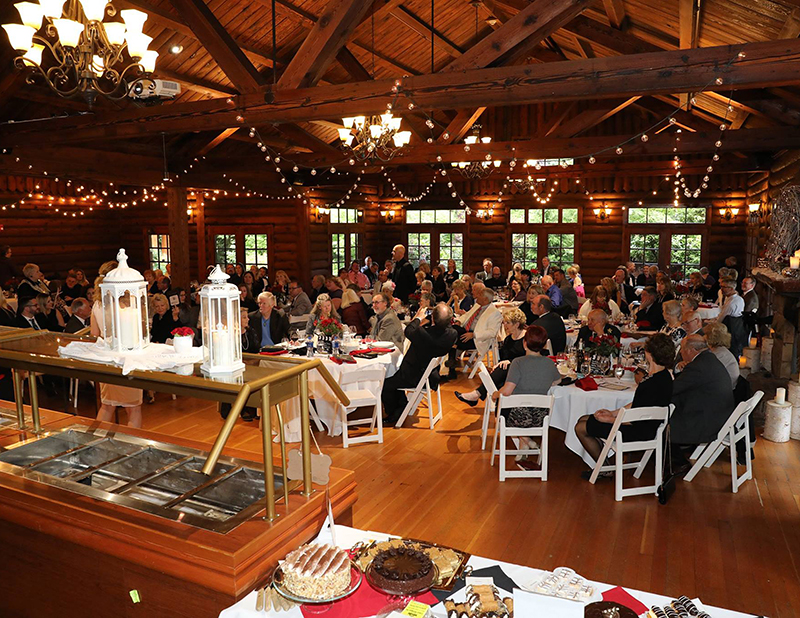 Indoor event, wooden room filled with tables, food and guests