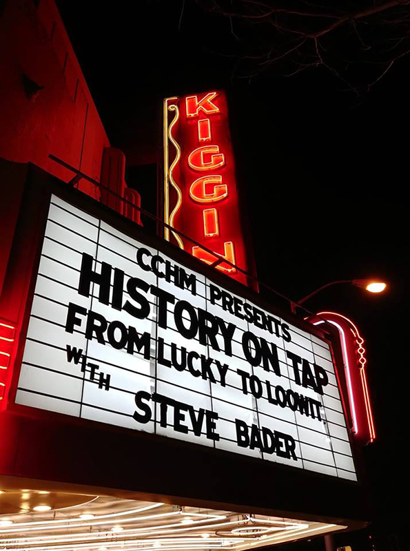 Outside Kiggins Theater marquee at night with neon lighting, black text “History on Tap”