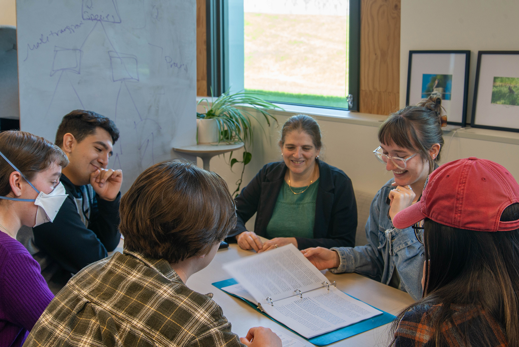 Three researchers in a laboratory setting, one working at a biological safety cabinet while the other two are standing nearby laughing and engaging.