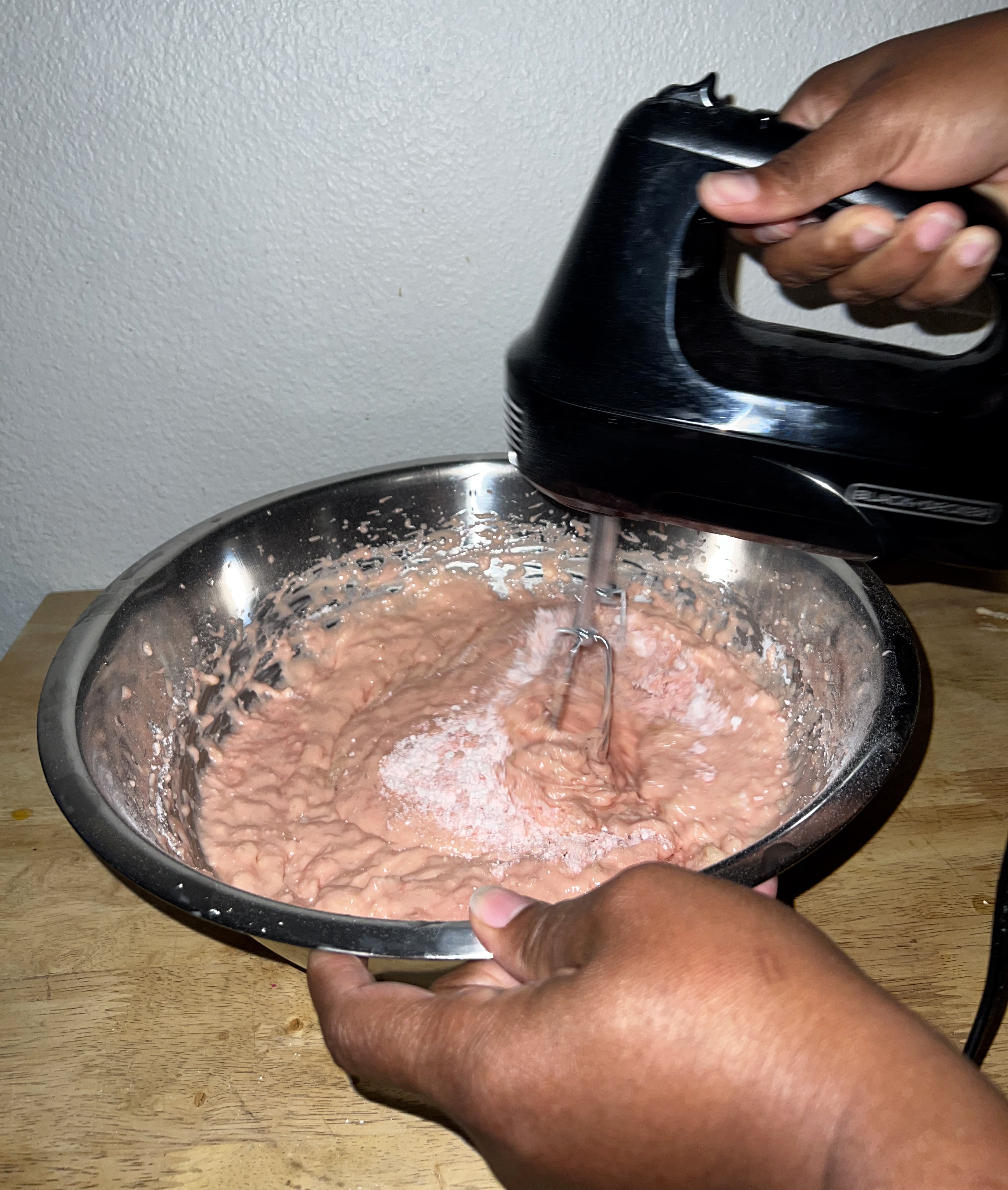 A picture of a hand blending strawberry cake mix with a blender.