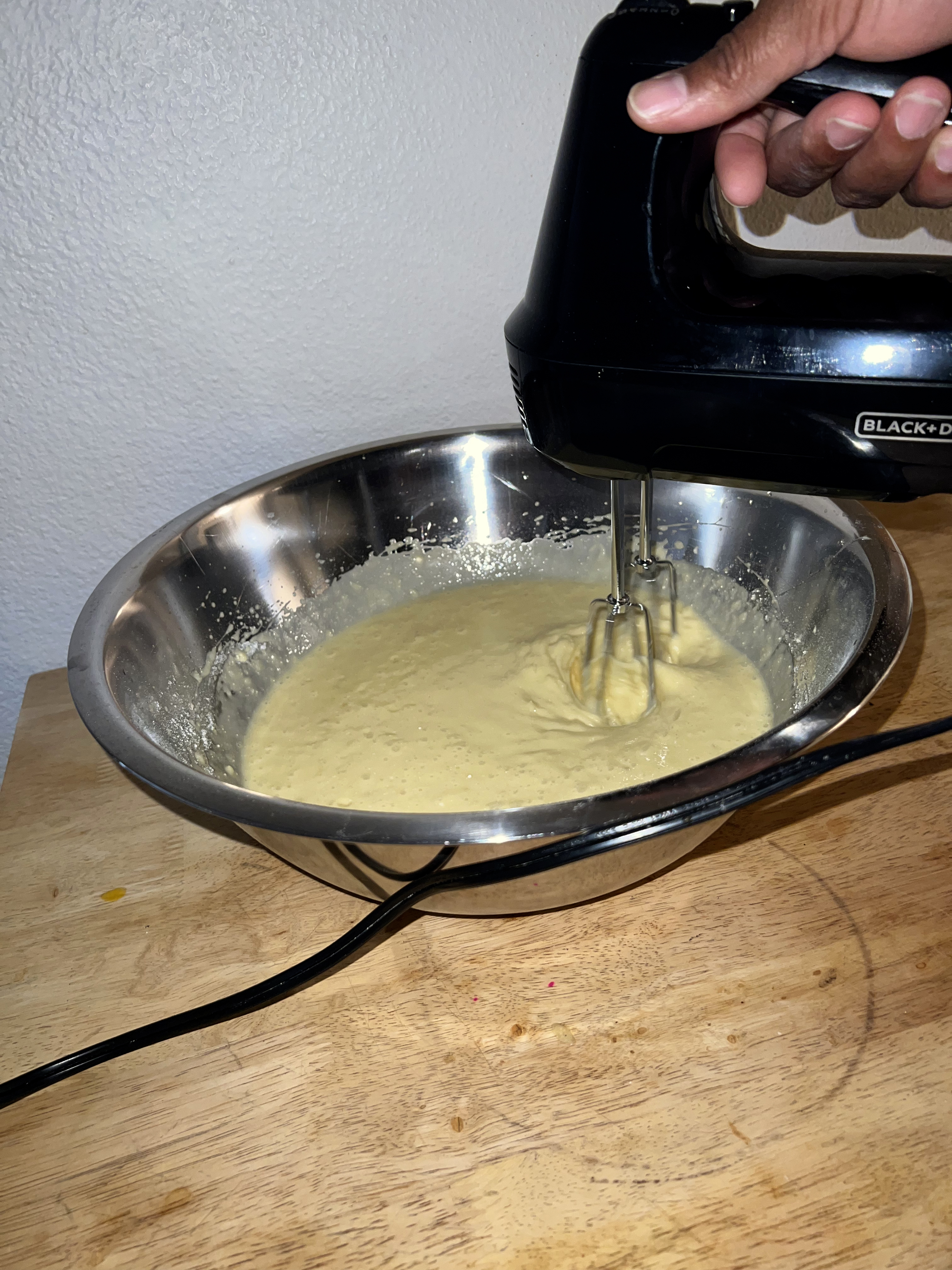 A picture of a hand blending pineapple cake mix with a blender.